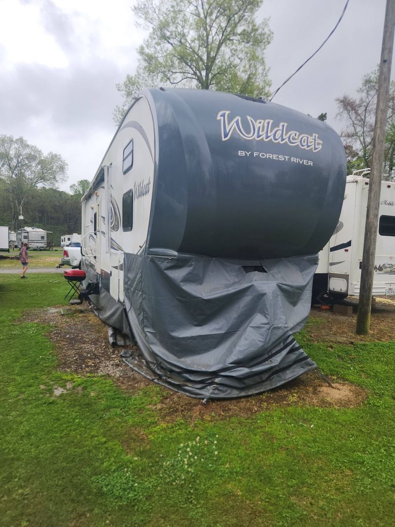 Black-and-gray travel trailer with covered front, parked on grass at an RV site