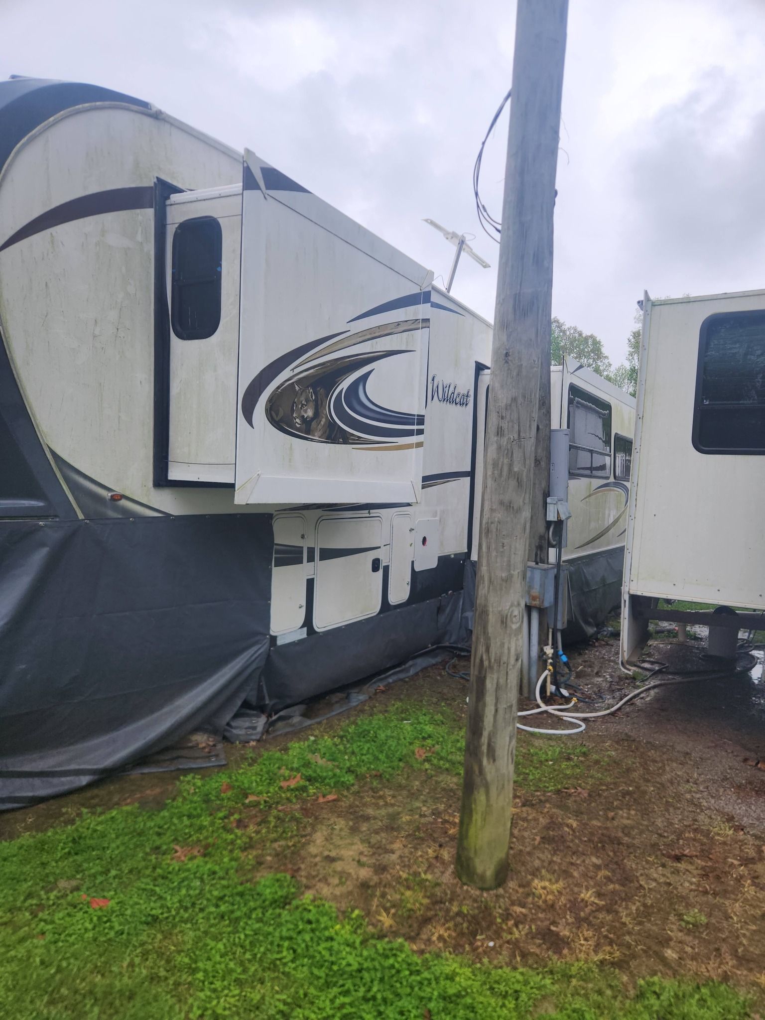 Two parked RVs with slide-outs squeezed beside a wooden utility pole on a muddy, grassy lot.