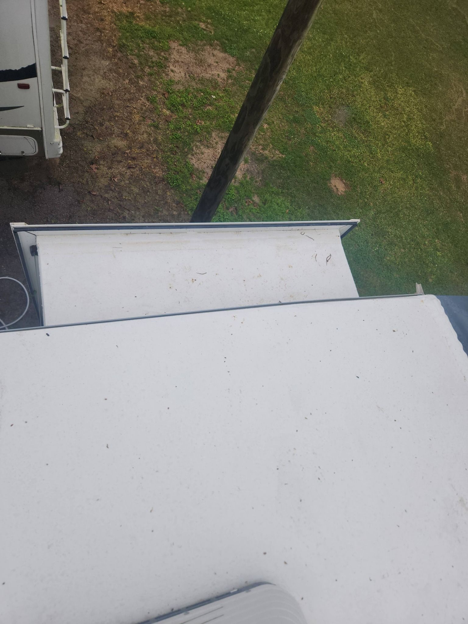 White rooftop and grassy yard seen from above with a dark pole in the center