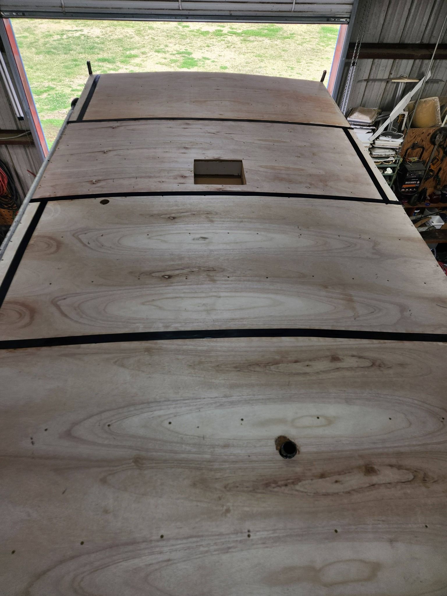 Wooden board surface with cracks and a small rectangular cutout, viewed inside a garage.