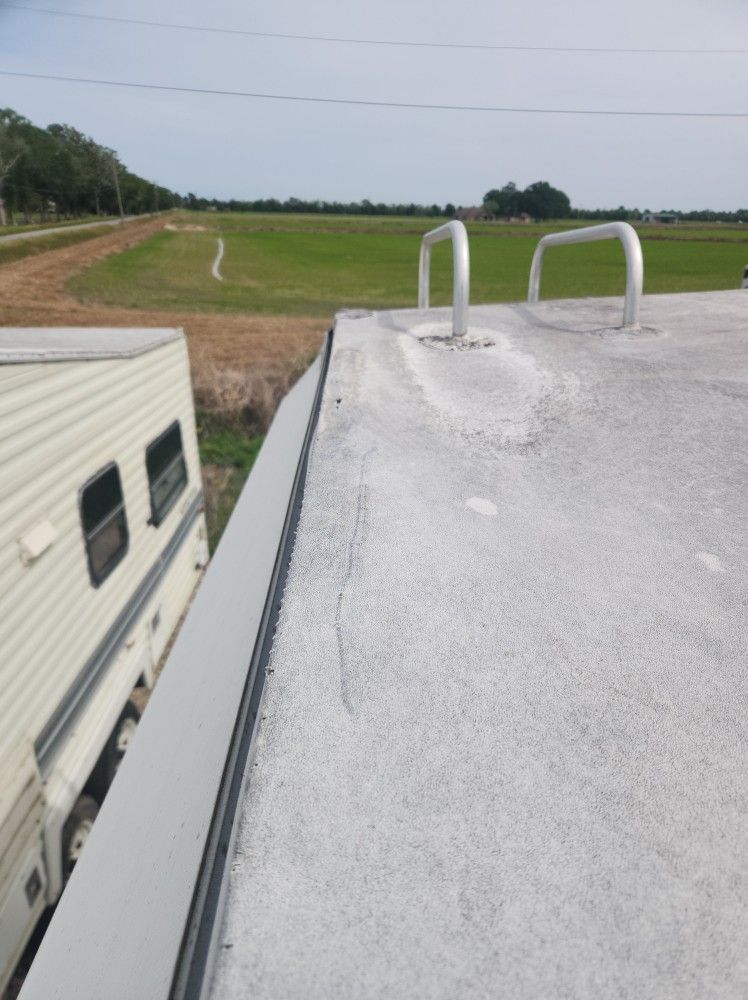 View from a camper roof overlooking a grassy field and a neighboring RV under a cloudy sky