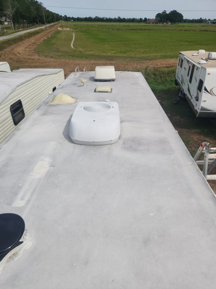 RV roof with white vents and skylight, overlooking a field and parked camper trailers