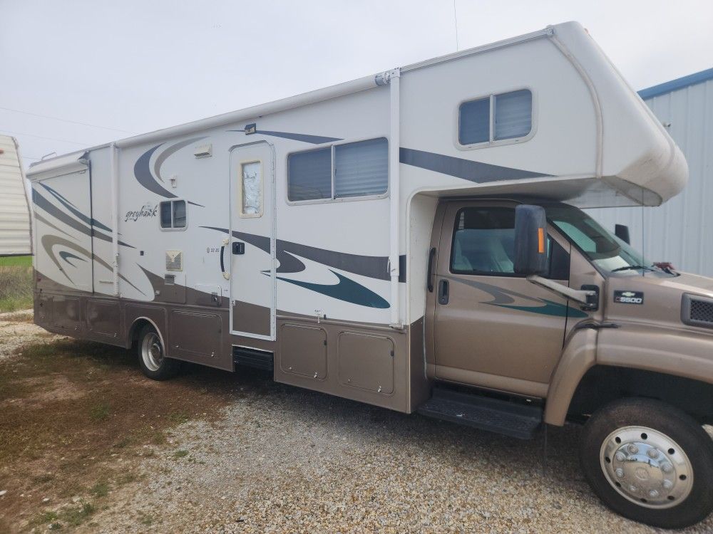 Beige and white cab-over RV parked on a dirt lot, side view