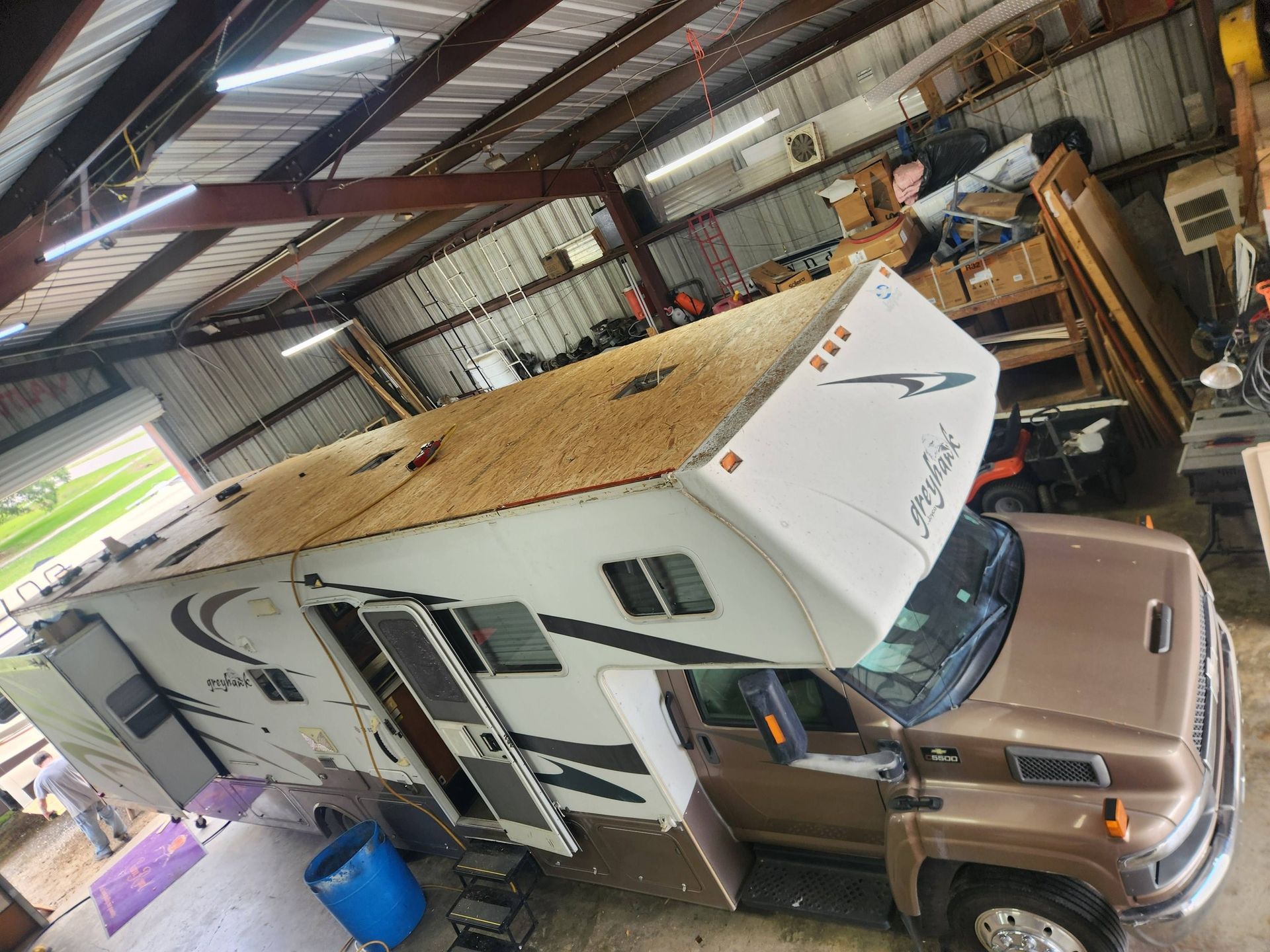 Camper trailer hitched to a tan truck inside a cluttered metal garage with tools and storage items