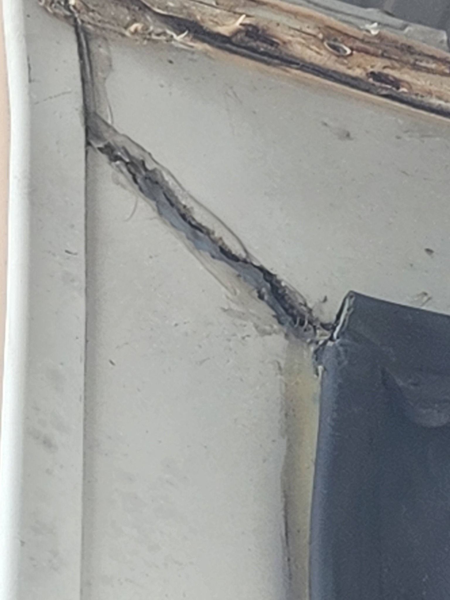 Damaged wall corner with a long diagonal crack and peeling paint near the ceiling