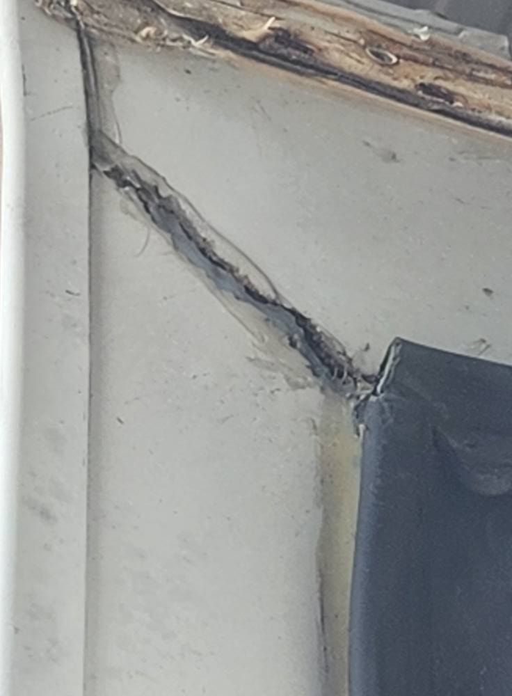 Cracked interior wall with a long diagonal fissure near a window frame and peeling trim