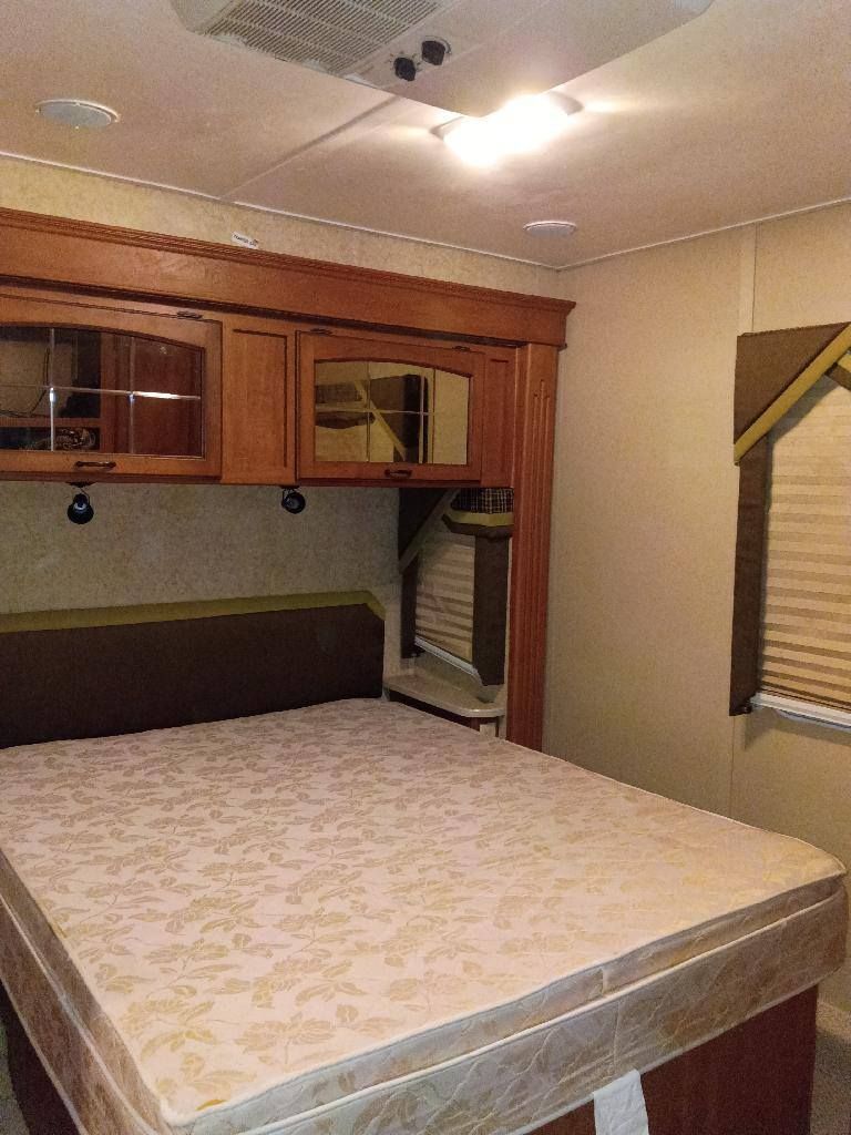 Small bedroom with a bed, overhead cabinets, and a window with blinds.