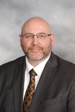 A bald man with a beard and glasses is wearing a suit and tie.