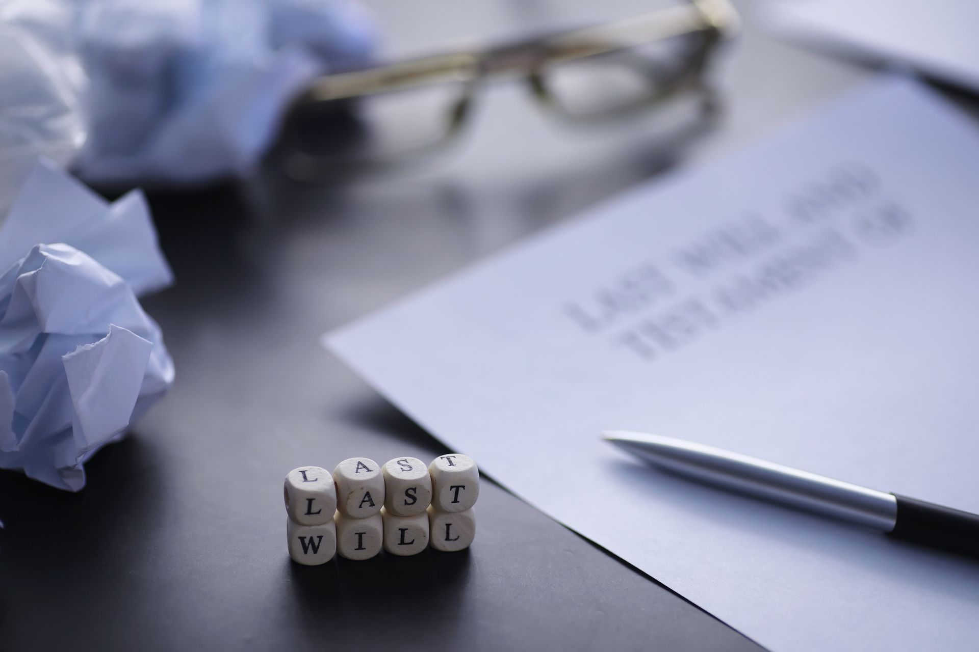 Last Will and Testament document with pen, glasses, crumpled paper, and word cubes 