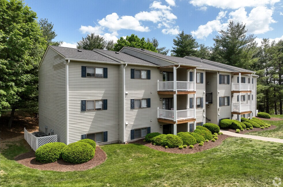 Apartment building with tan siding, balconies, and landscaping on a grassy hill under a blue sky.