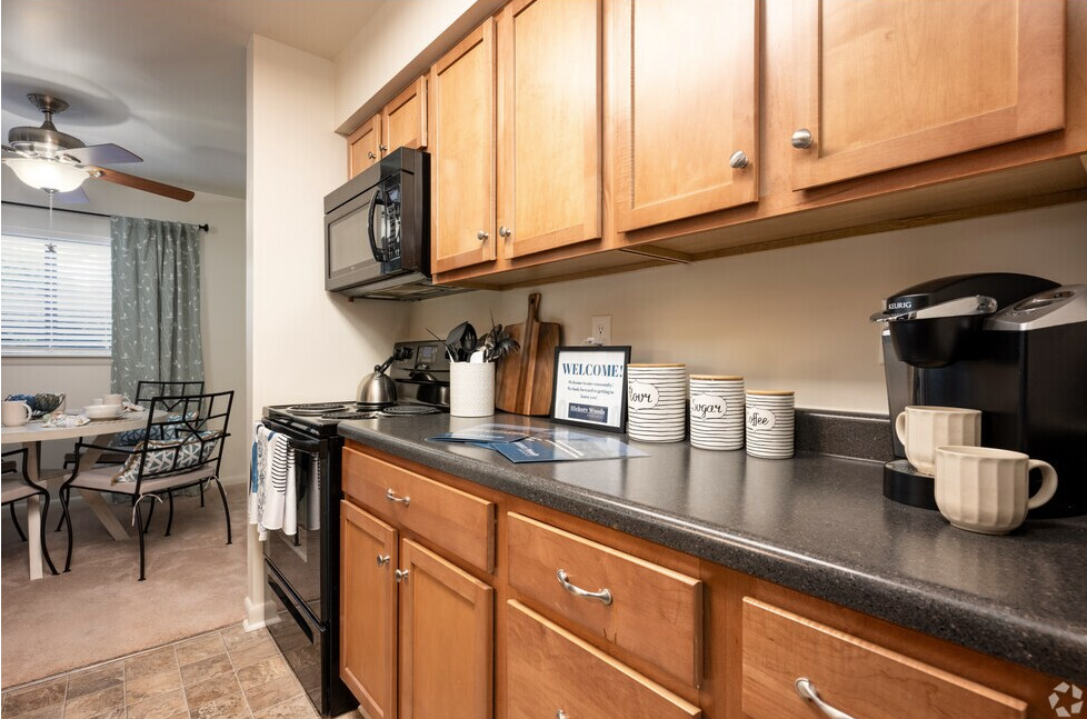 Kitchen with wooden cabinets, microwave, stove, coffee maker, and dining area in the background.