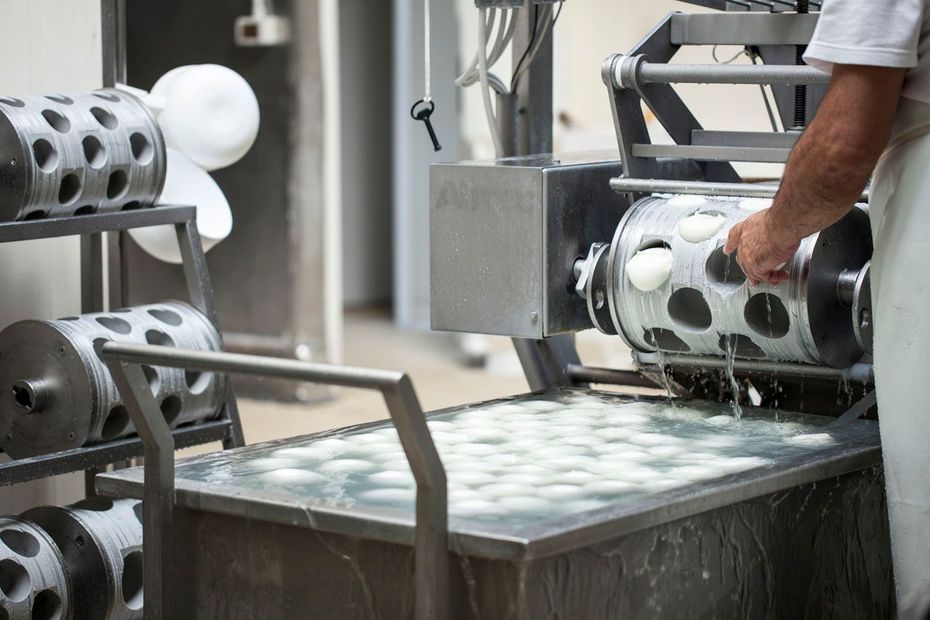 Operaio che movimenta cilindri metallici perforati in una stazione di lavorazione industriale.