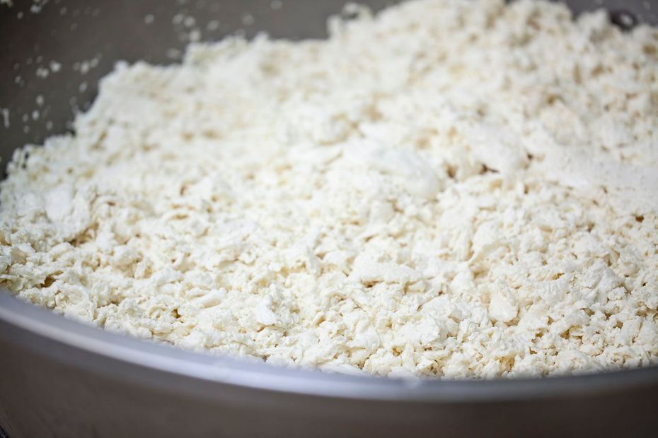 Primo piano di una ciotola piena di formaggio bianco sbriciolato o cagliata.
