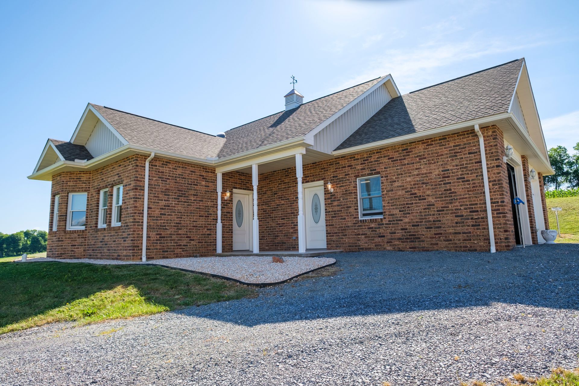 Brick house with white trim and a gravel driveway under a bright blue sky