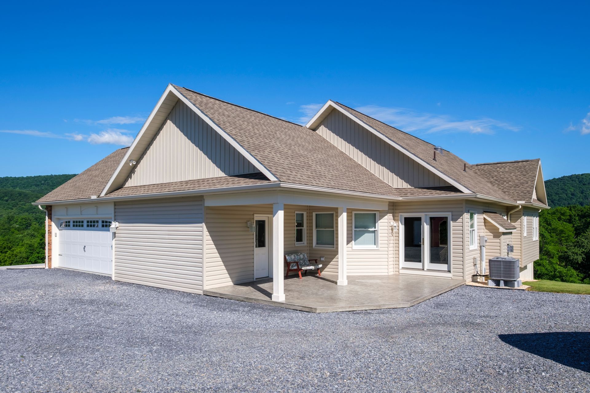 Single-story beige house with a gravel driveway and attached garage under a blue sky