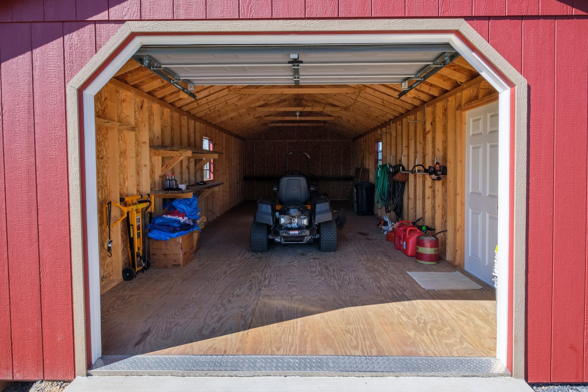 Open garage with a tractor inside, wooden walls, tools, and a red exterior frame