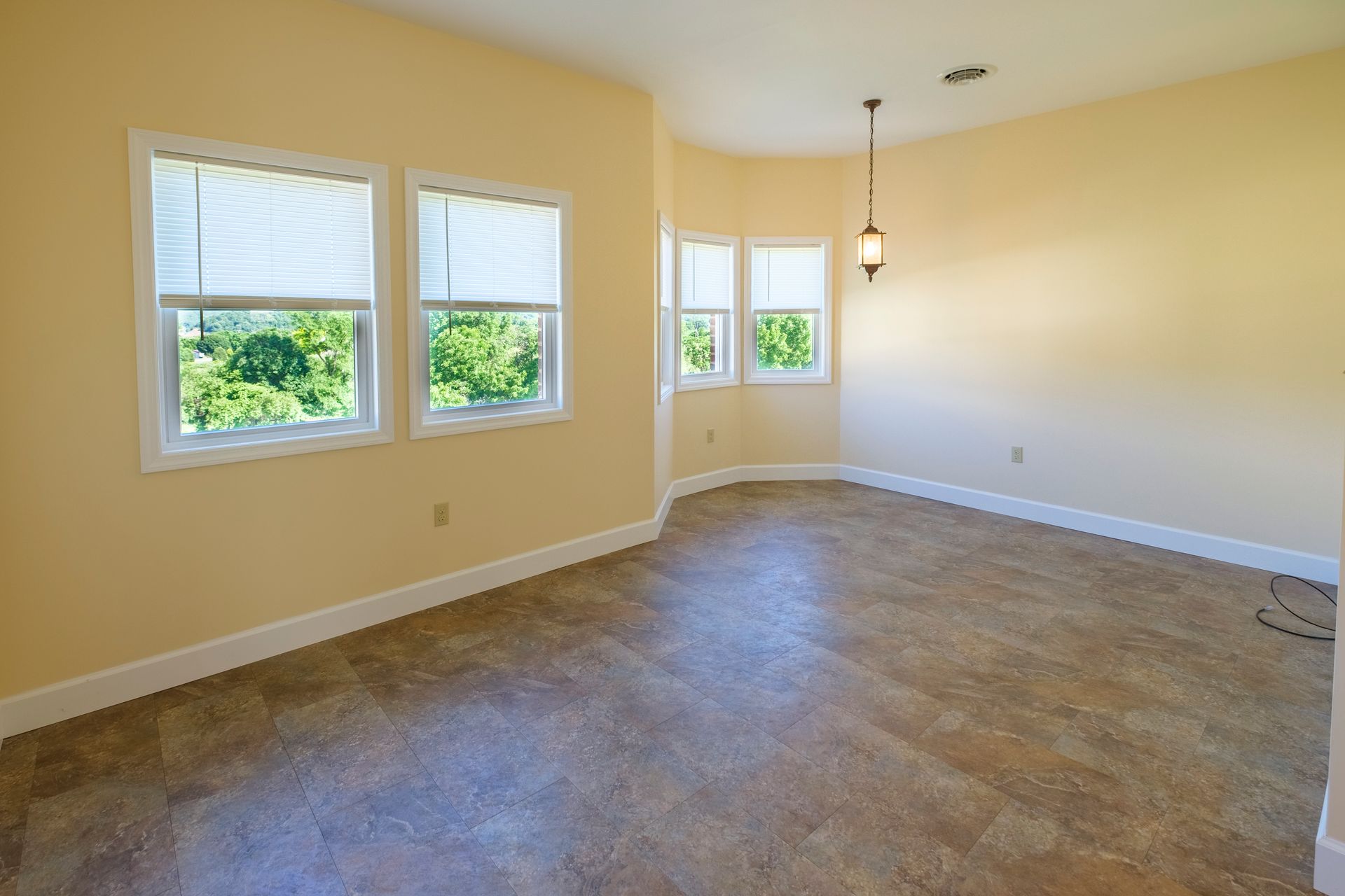 Empty beige living room with carpet, white trim, and three windows with blinds open to greenery