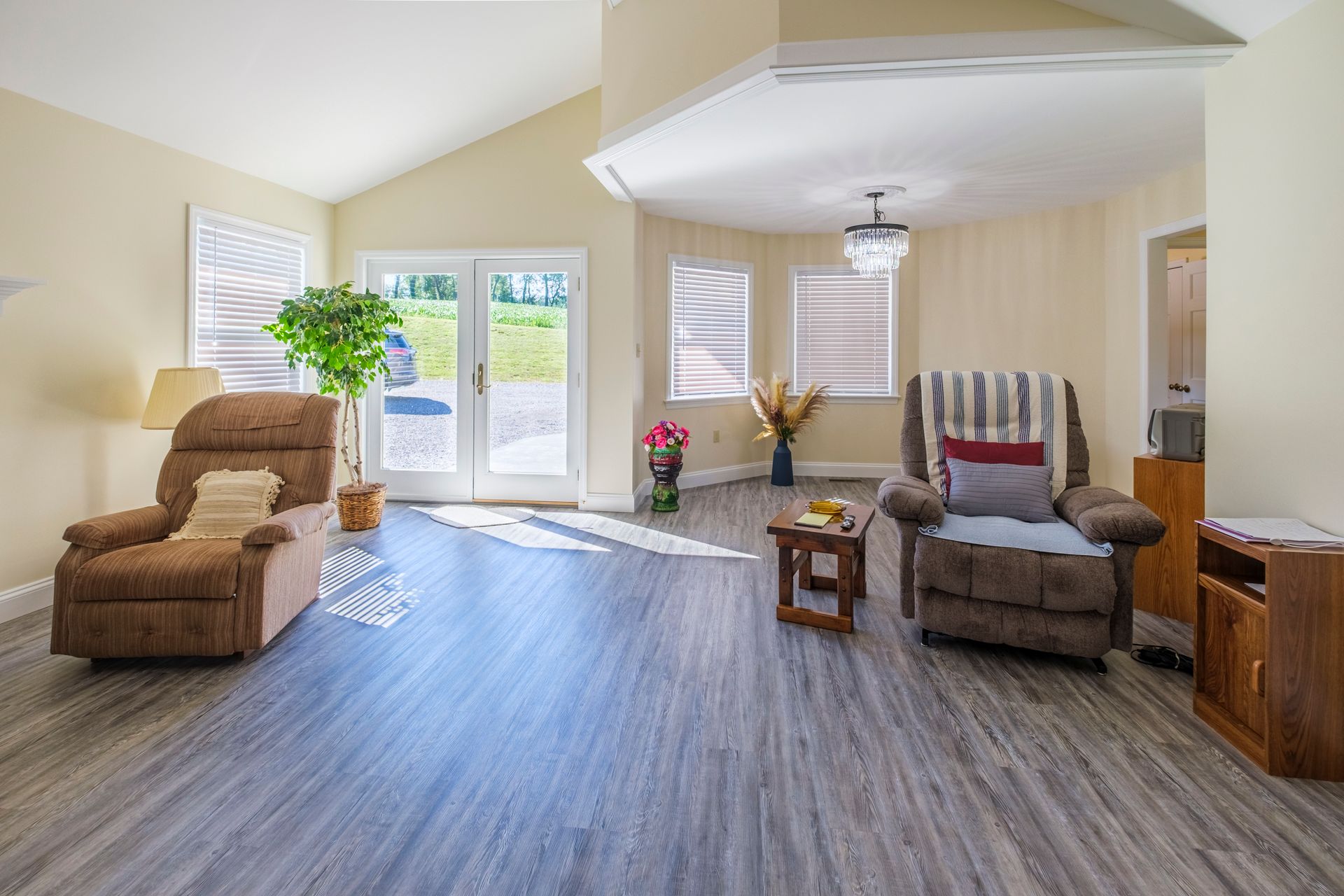 Bright living room with recliners, wood-look floor, and sunlight through large windows