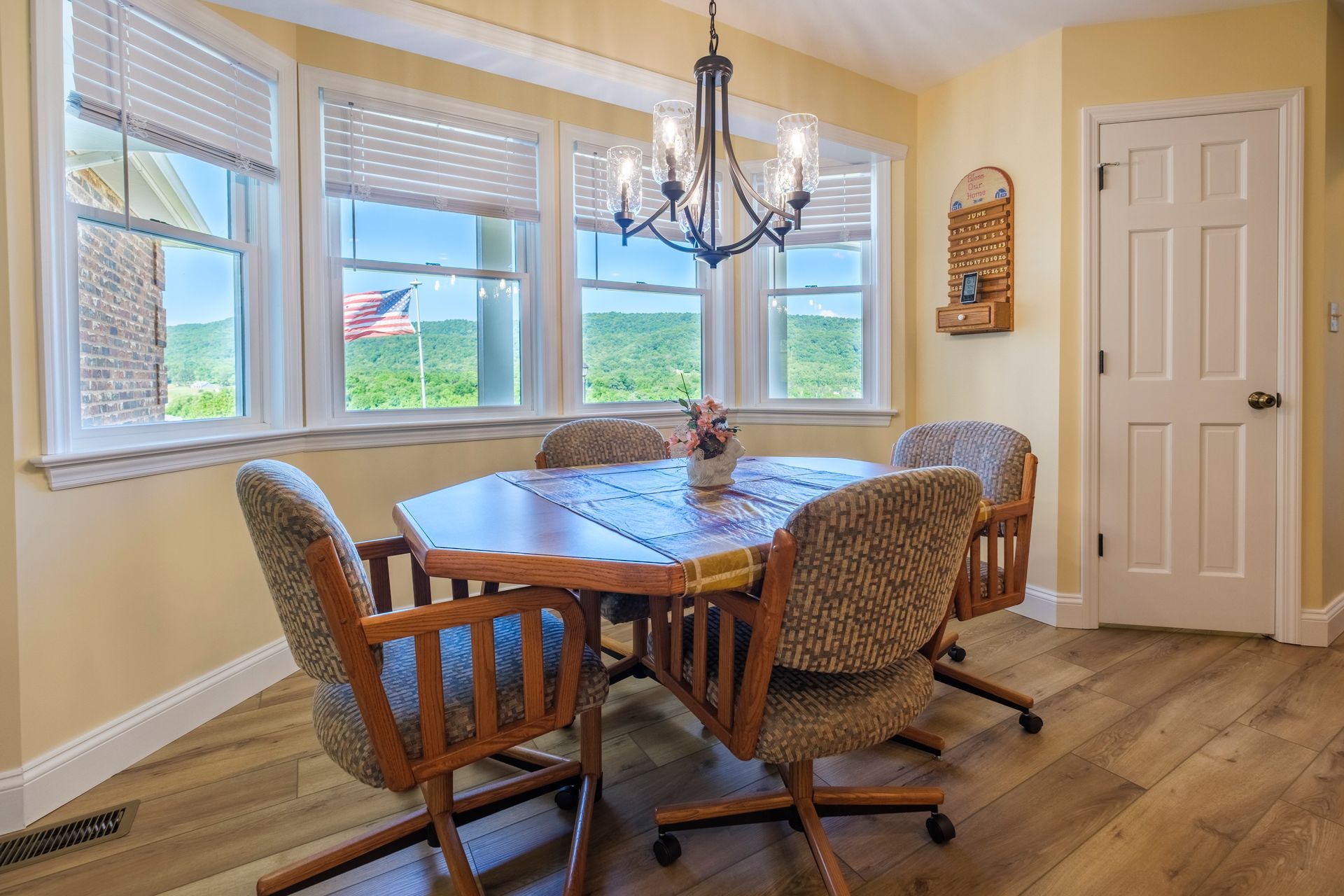 Bright dining room with a wooden table, patterned chairs, chandelier, bay windows, and hardwood floor