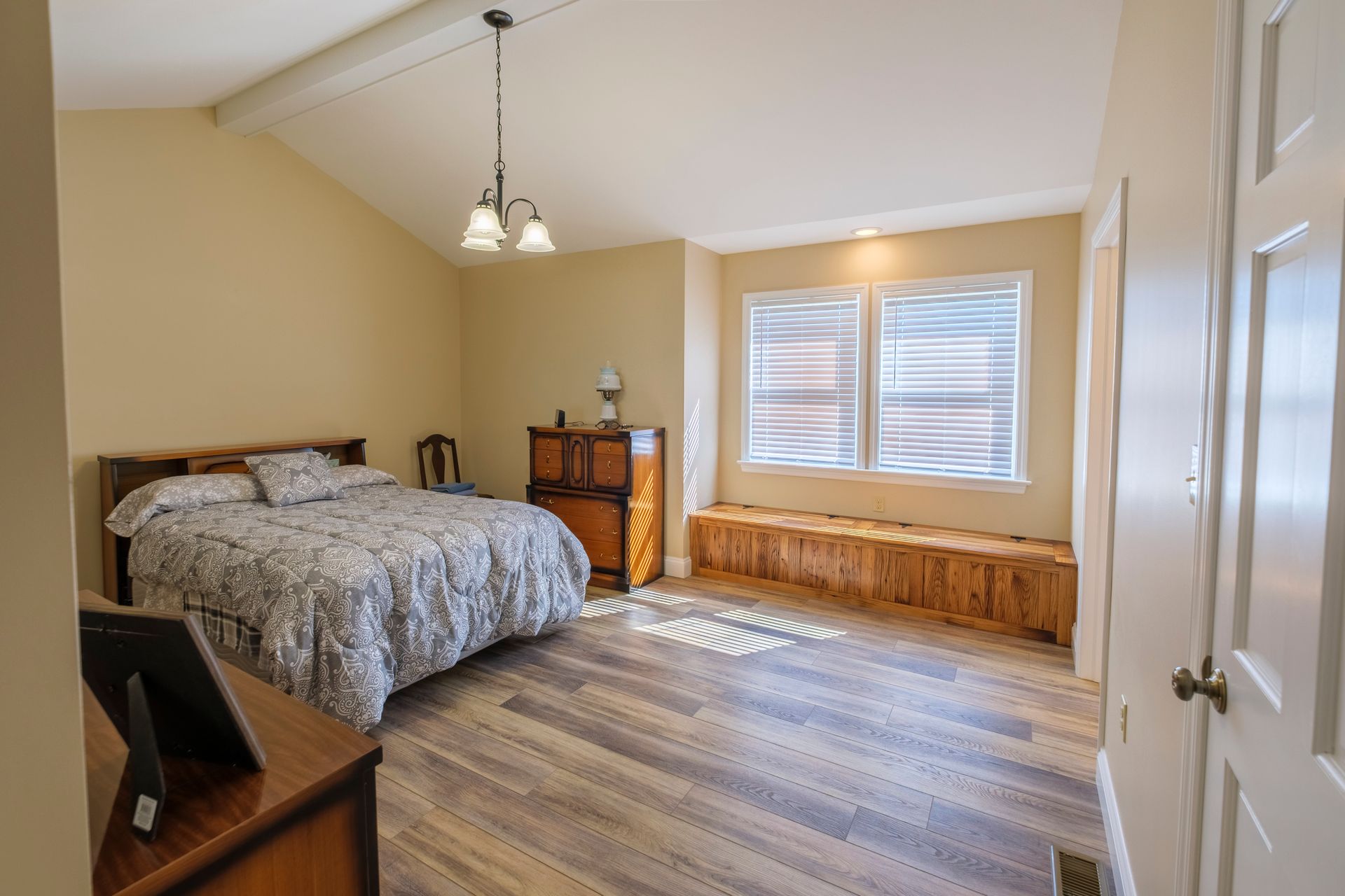 Bedroom with sloped ceiling, bed, wood dresser, bay window seat, and hardwood floors.