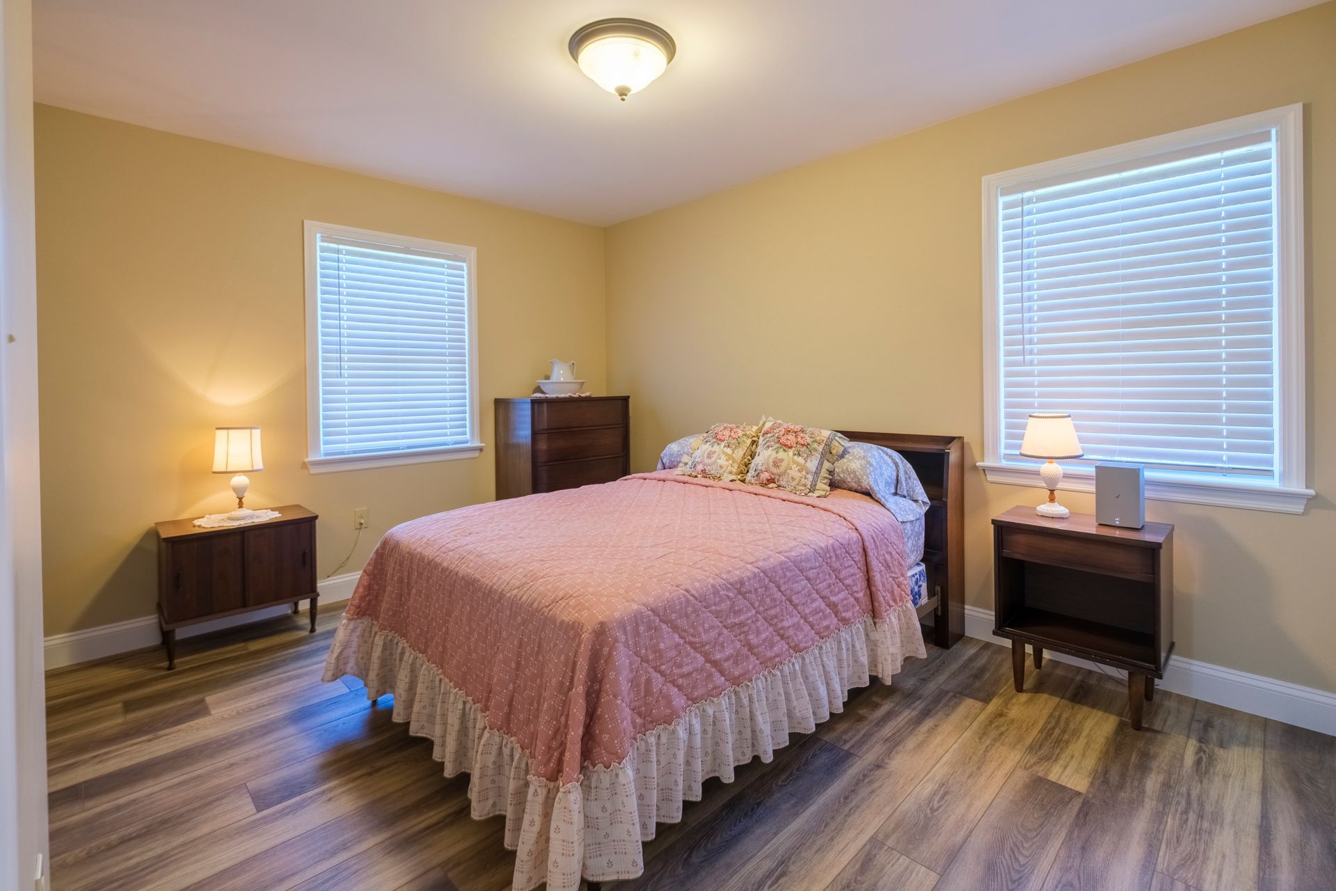 Bedroom with a bed, nightstands, lamps, and windows with blinds in a beige room.