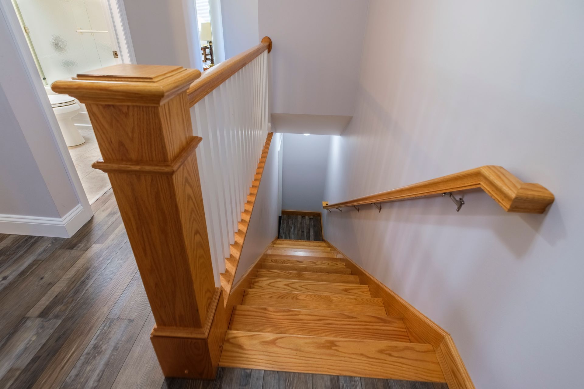 Wooden staircase with white walls, railings, and a carpeted landing, viewed from the top down.