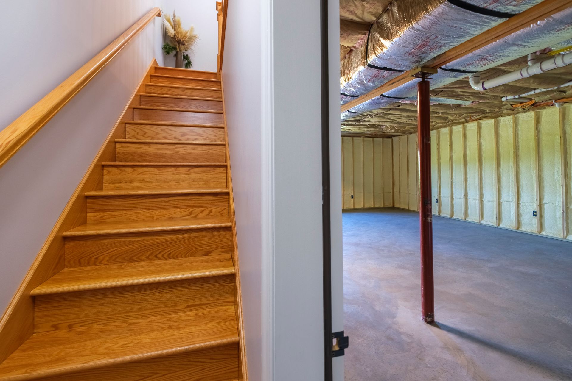 Basement stairs beside an unfinished utility room with exposed beams and concrete floor