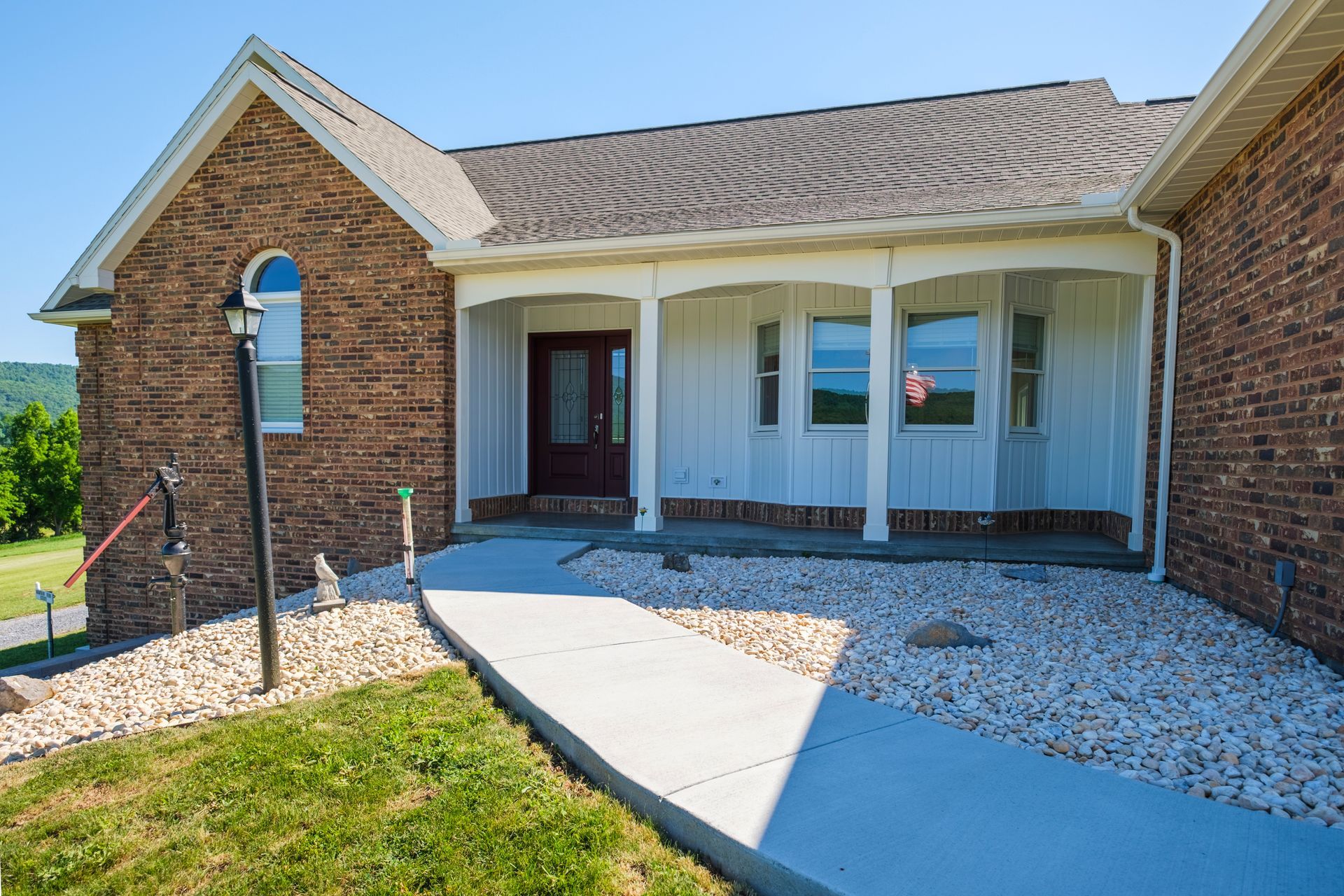Brick house entrance with white front porch, curved walkway, and gravel landscaping