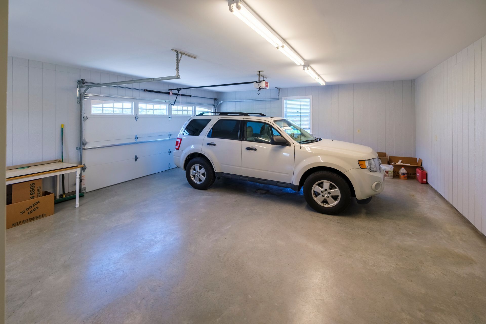 White SUV parked in a clean, empty garage with concrete floor and fluorescent lights.