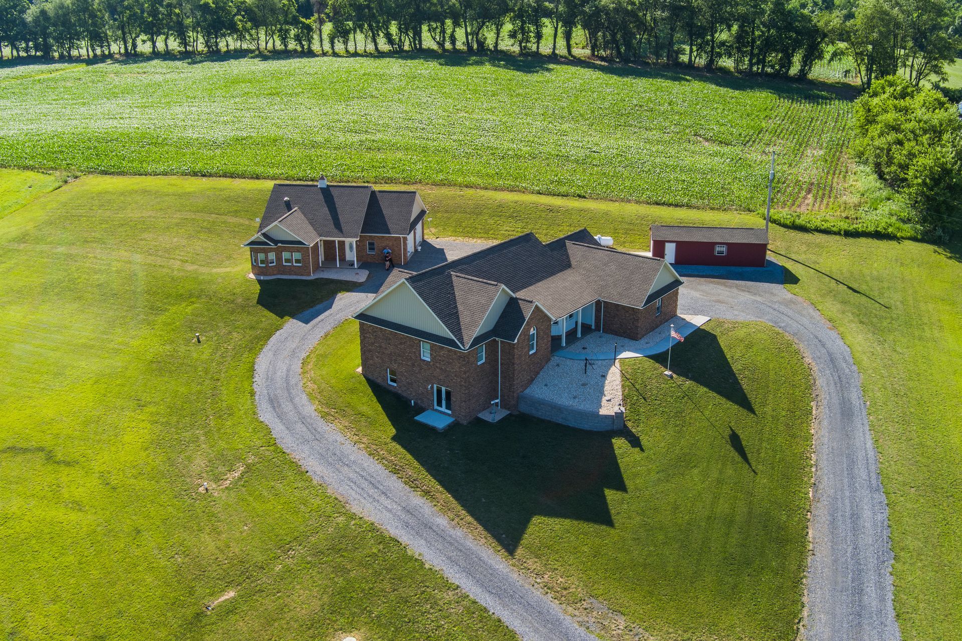 Aerial view of a large brick house with a curved driveway and green lawn surrounded by trees