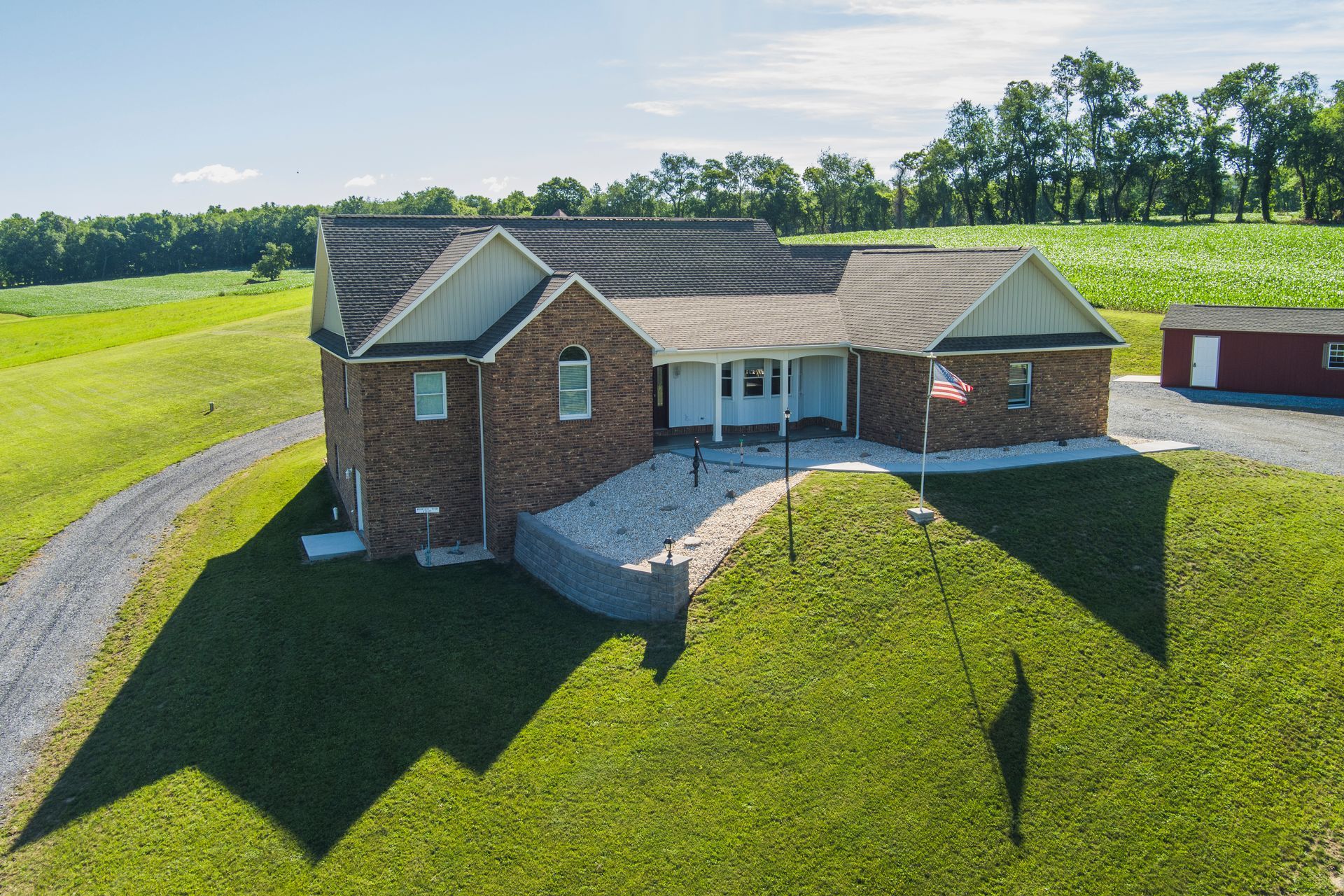 Brick ranch house with front porch and detached garage on a grassy rural lot under a clear sky