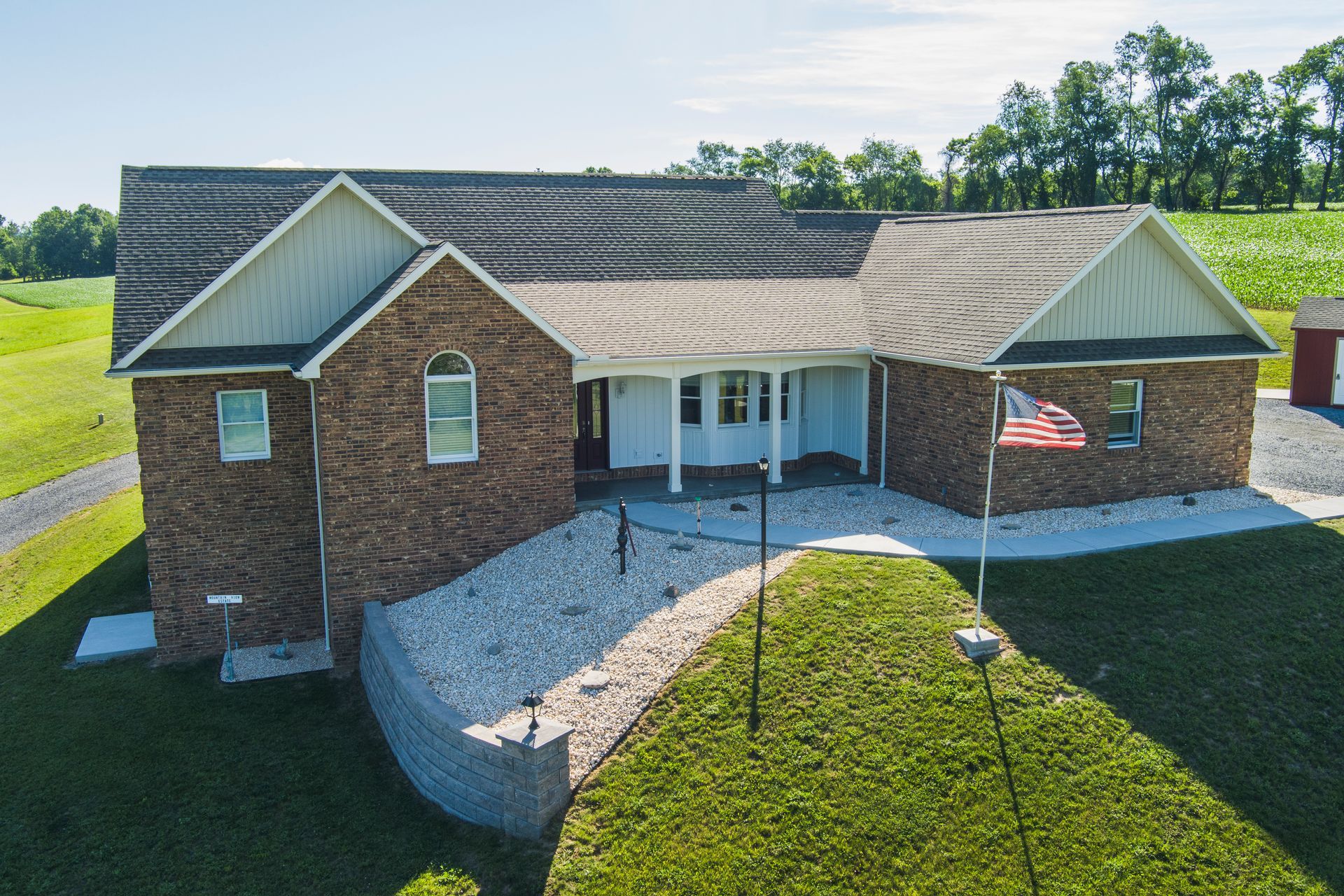 Brick suburban house with a white porch, curved walkway, and an American flag in the front yard