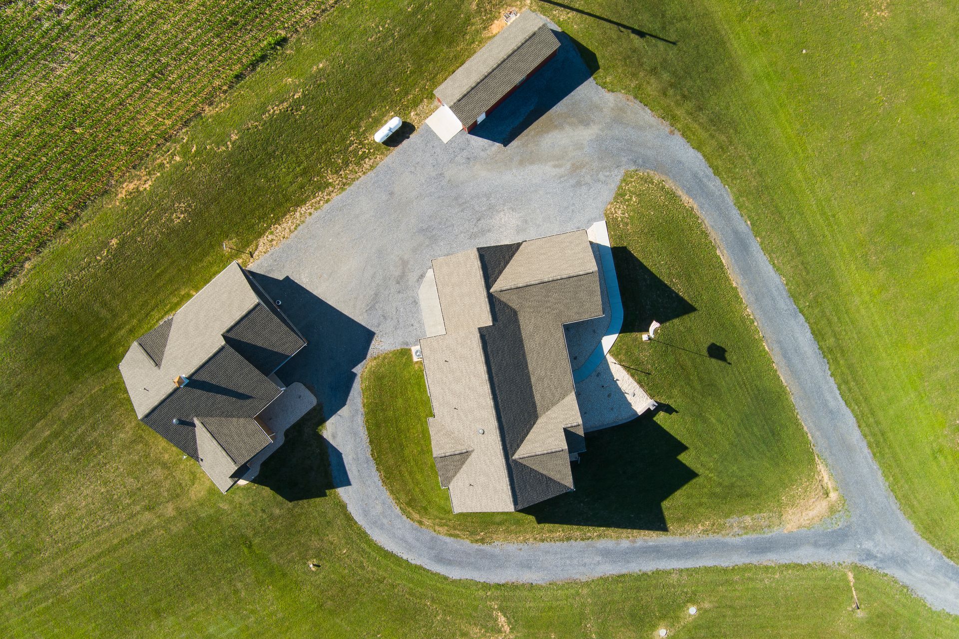 Aerial view of three houses, a shed, and curved gravel drive surrounded by green grass.