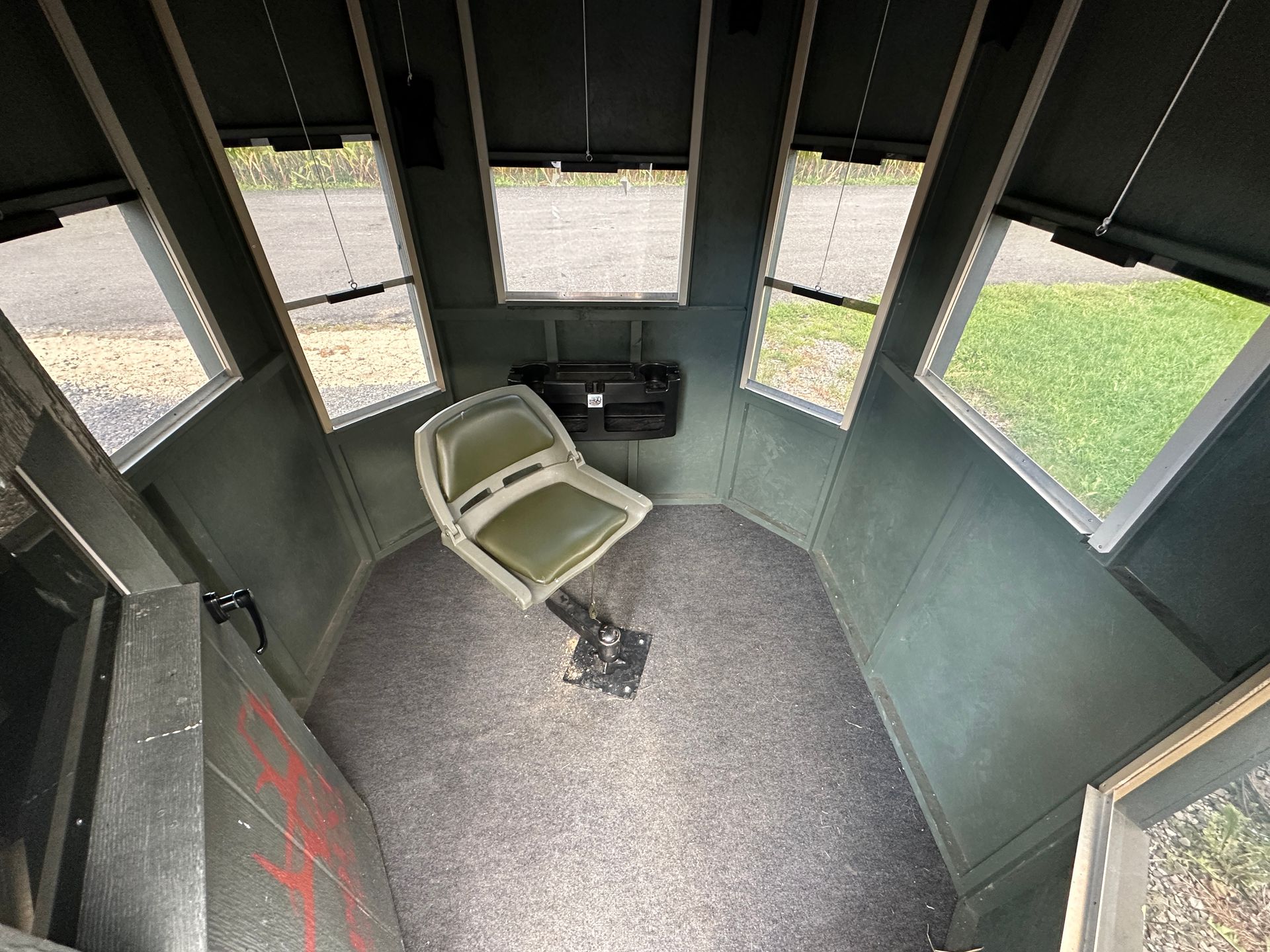 Inside a small green hunting blind with window openings and a folding chair on the floor.