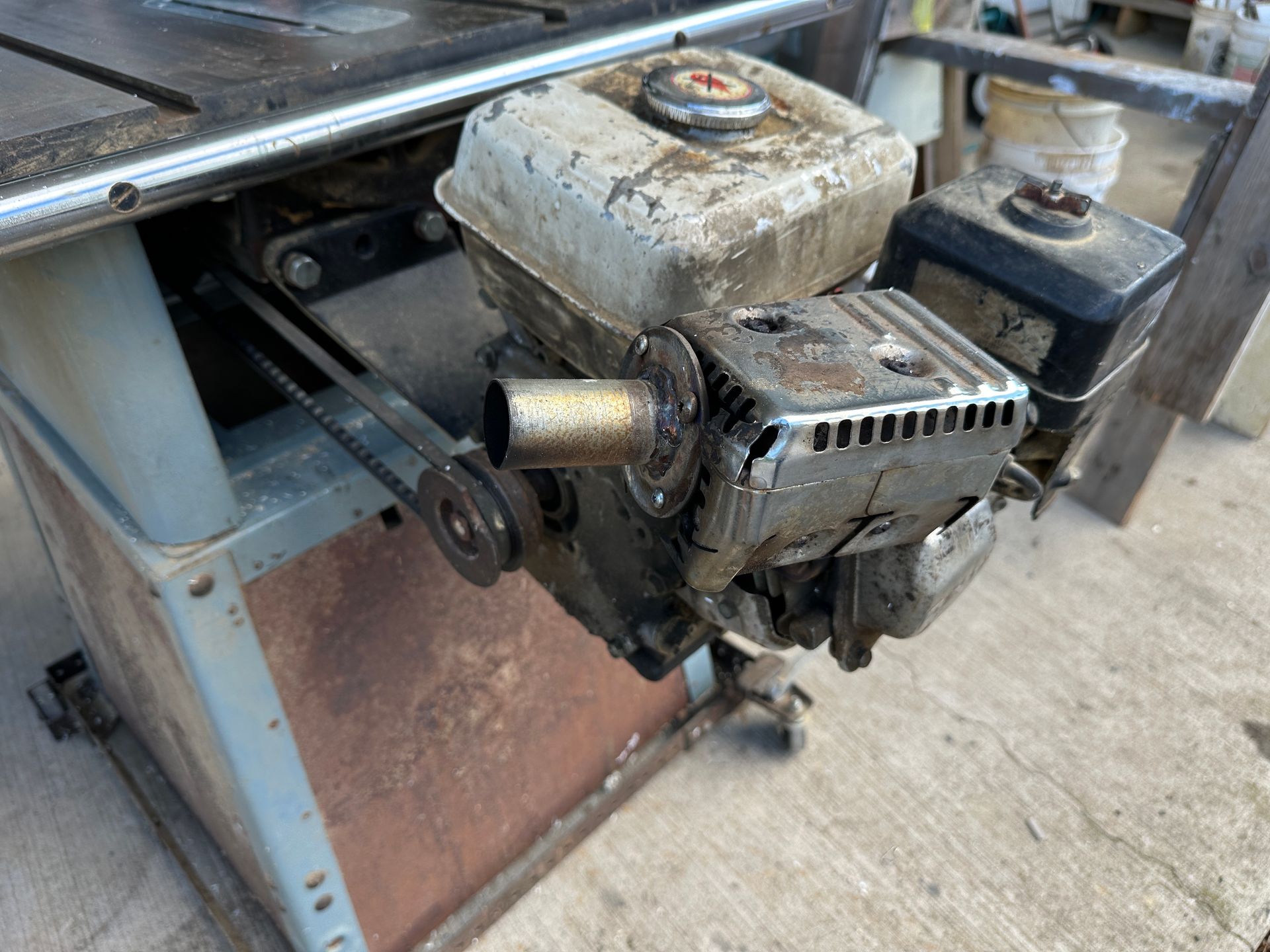 Close-up of a worn small engine mounted on rusty industrial machinery outdoors.