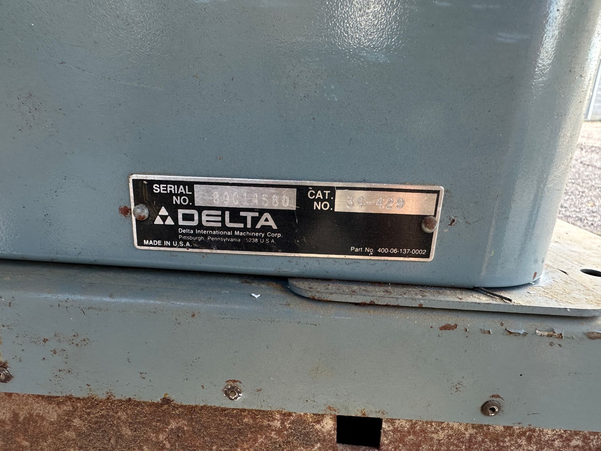 Close-up of a worn blue Delta machine label plate on a metal surface.