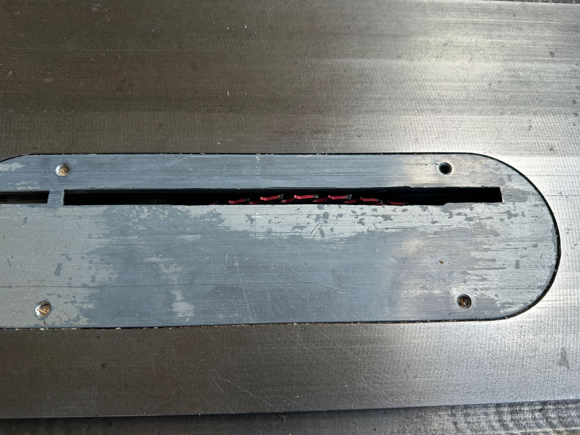 Worn metal panel with a long narrow slot and four screws on a gray surface