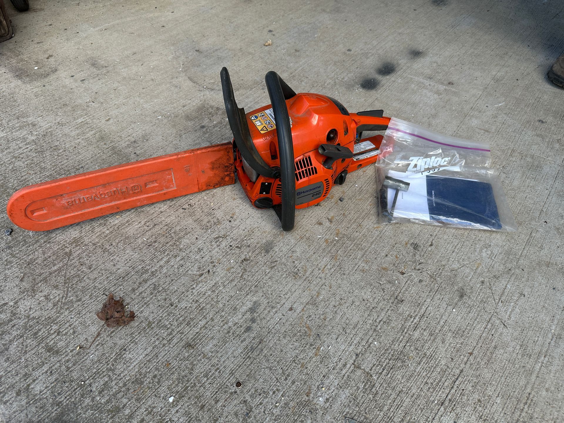 Orange chainsaw on concrete with a clear plastic bag of accessories beside it