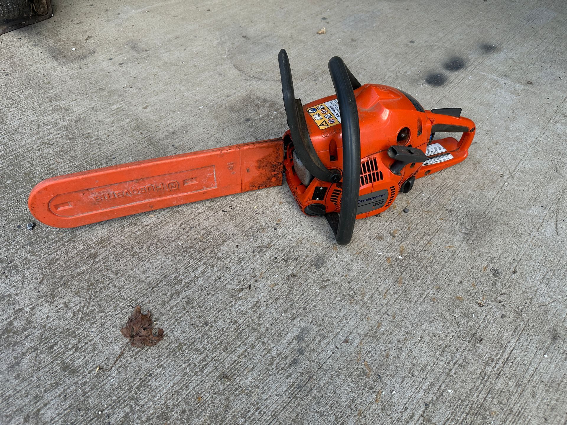 Orange chainsaw lying on concrete pavement with blade cover attached