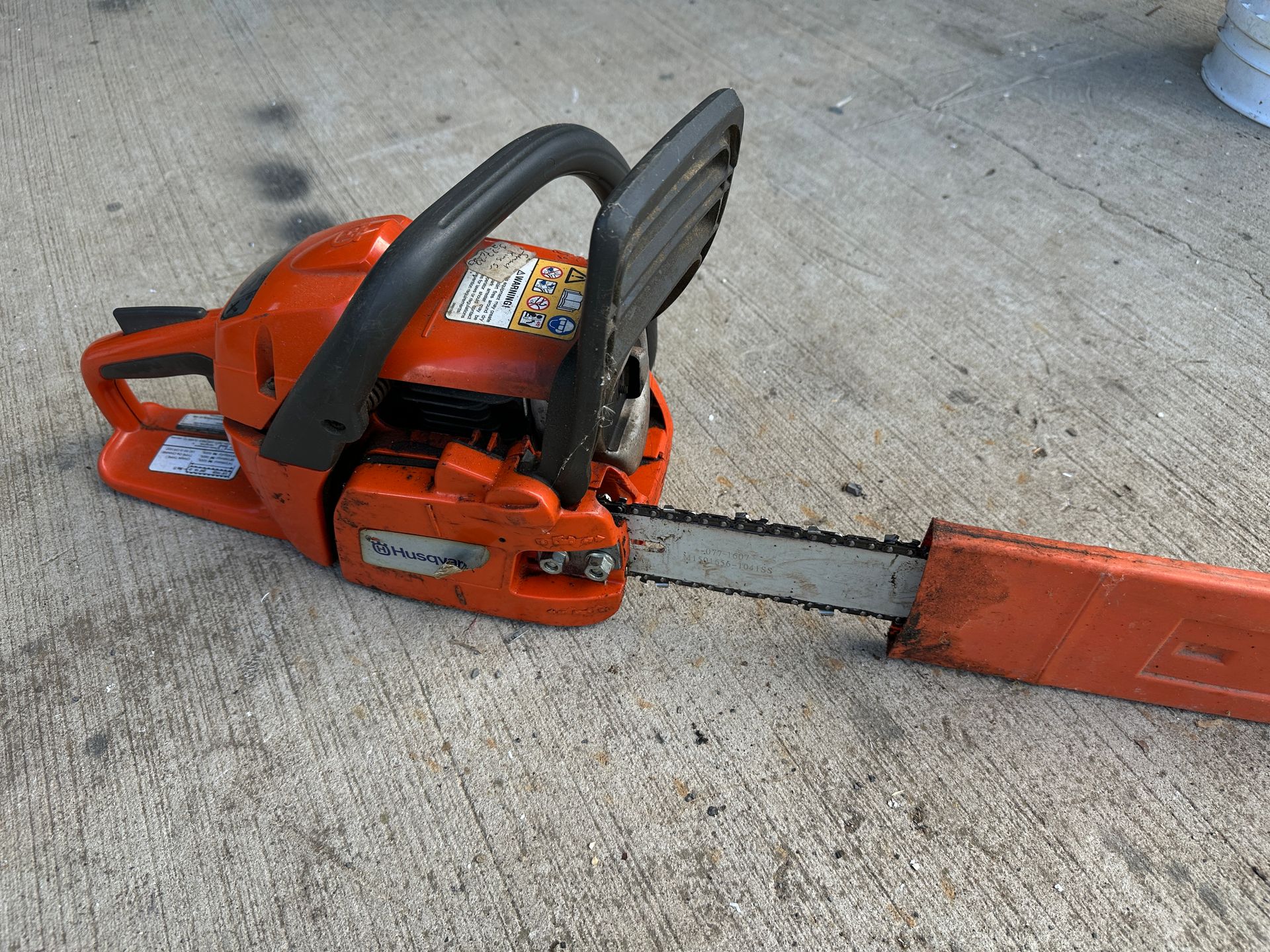 Orange chainsaw on concrete, with bar and blade cover attached.