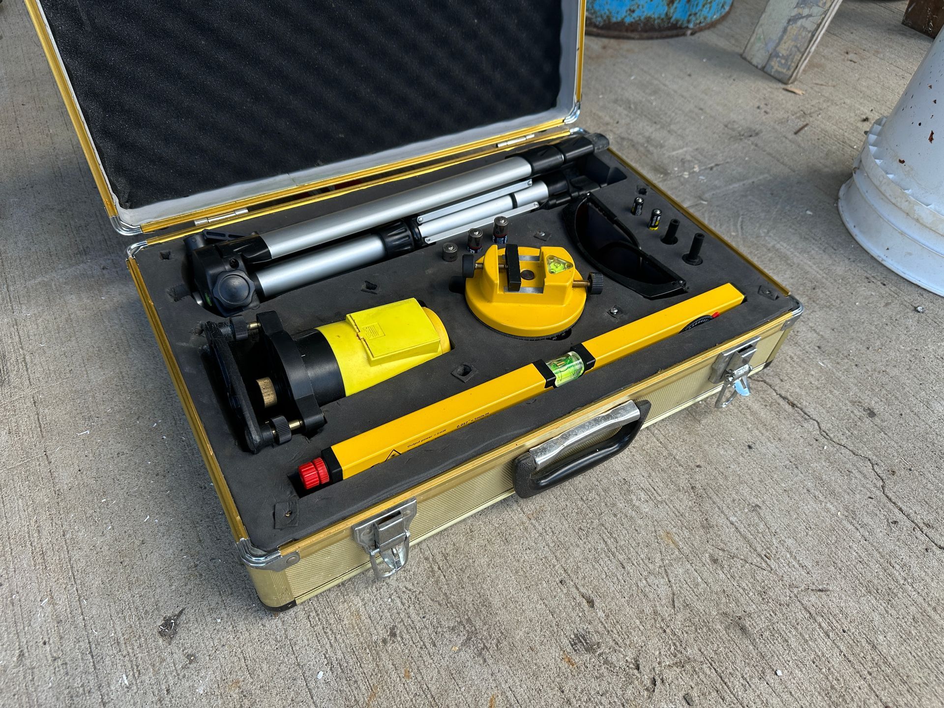 Open toolbox with yellow-and-black tools and a long silver cylinder on a concrete floor