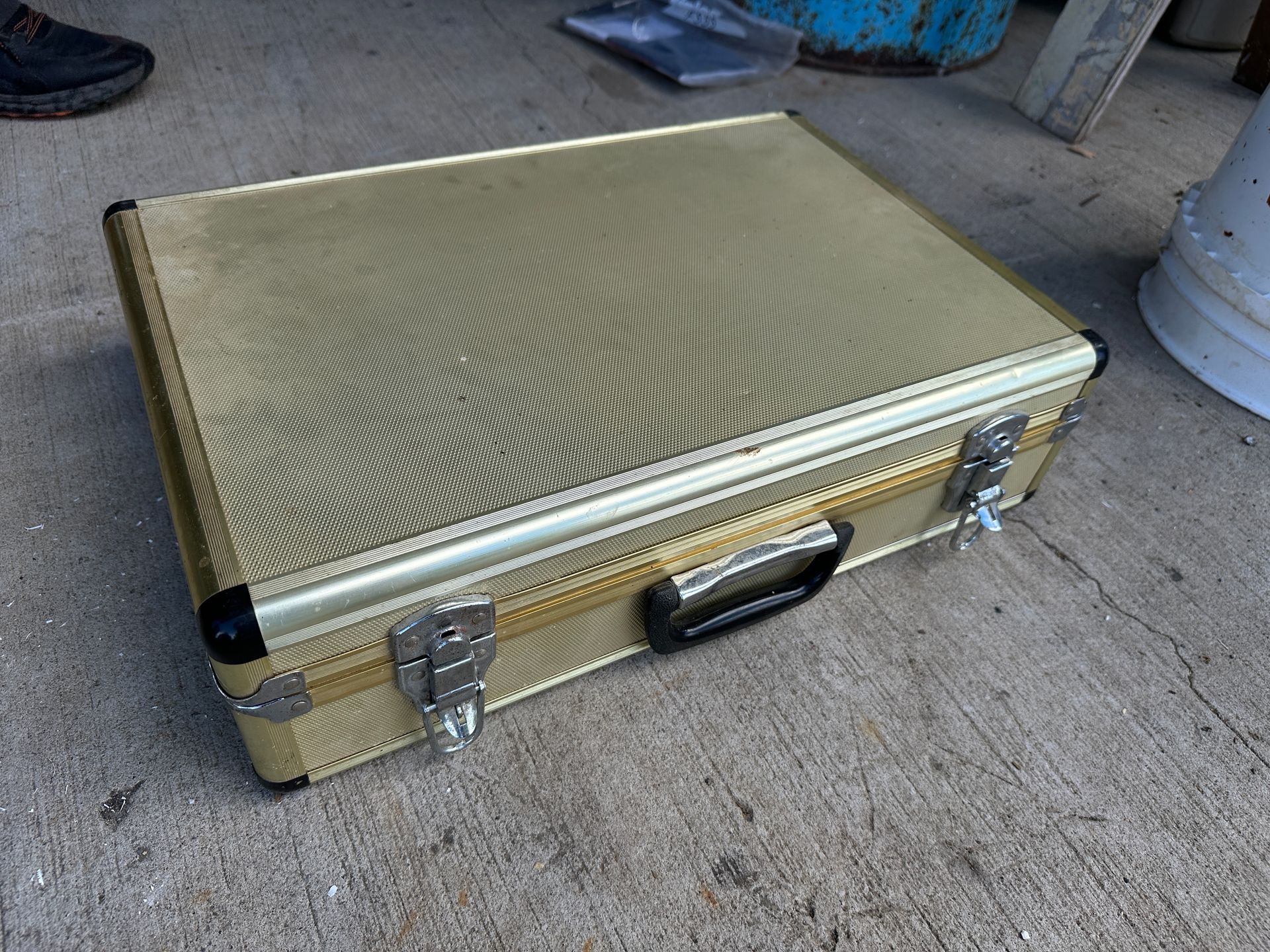 Gold textured suitcase on concrete ground with metal latches and black handle