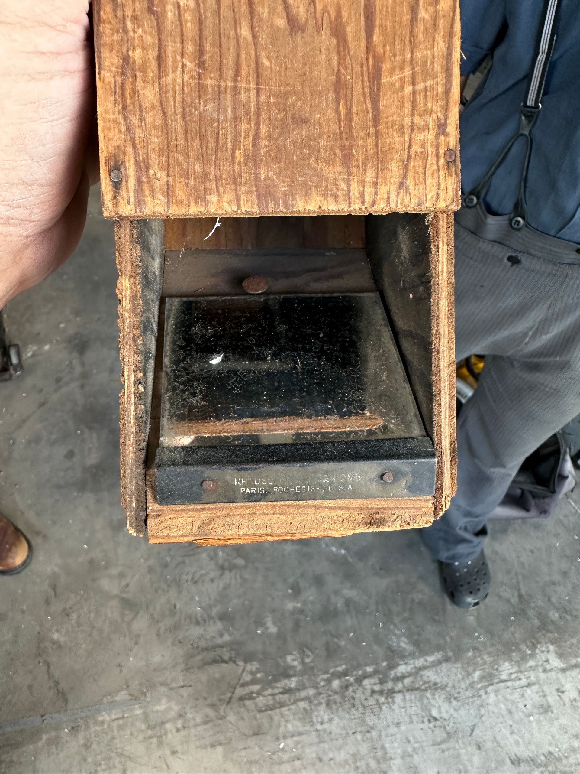 Rusty metal box with an open front, held by people on a concrete floor.