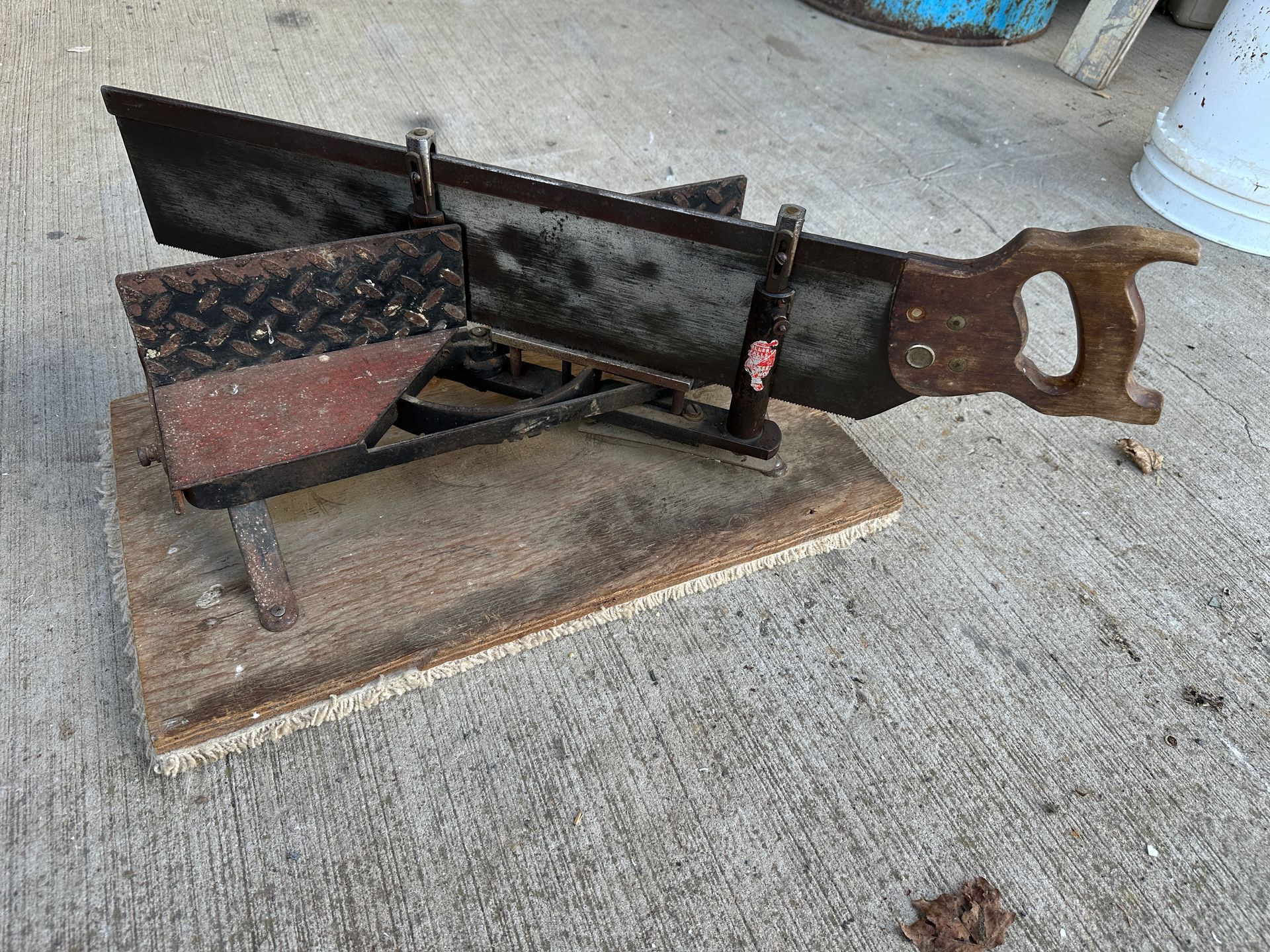 Rusty old mechanical device on a concrete surface outdoors, with a long handle and wooden base