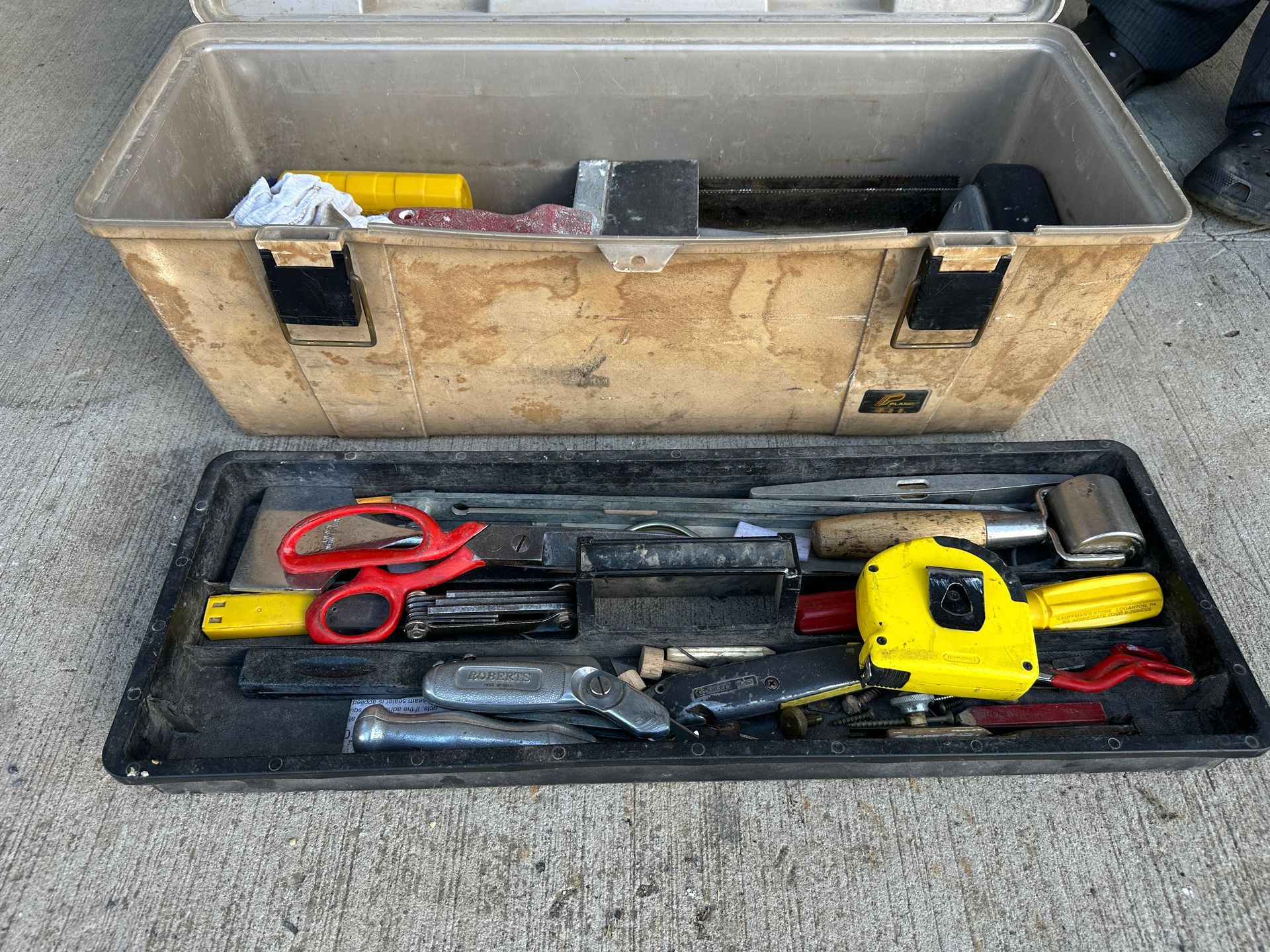 Open tool case with assorted hand tools and red scissors laid out on a black tray.