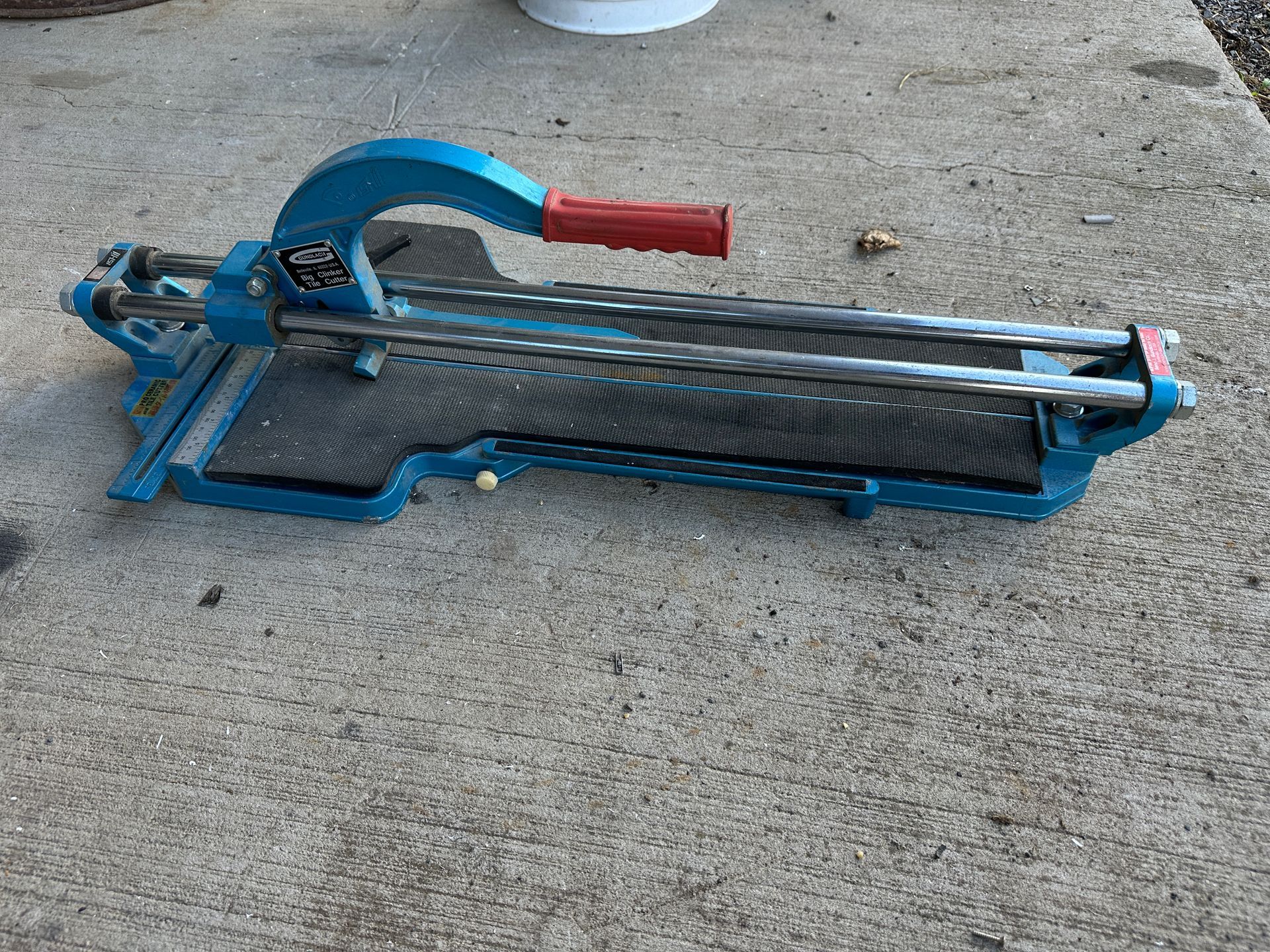 Blue tile cutter with red handle resting on concrete.