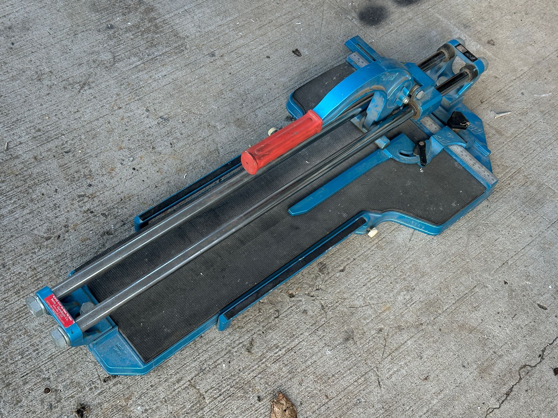 Blue tile cutter with red handle on a concrete surface