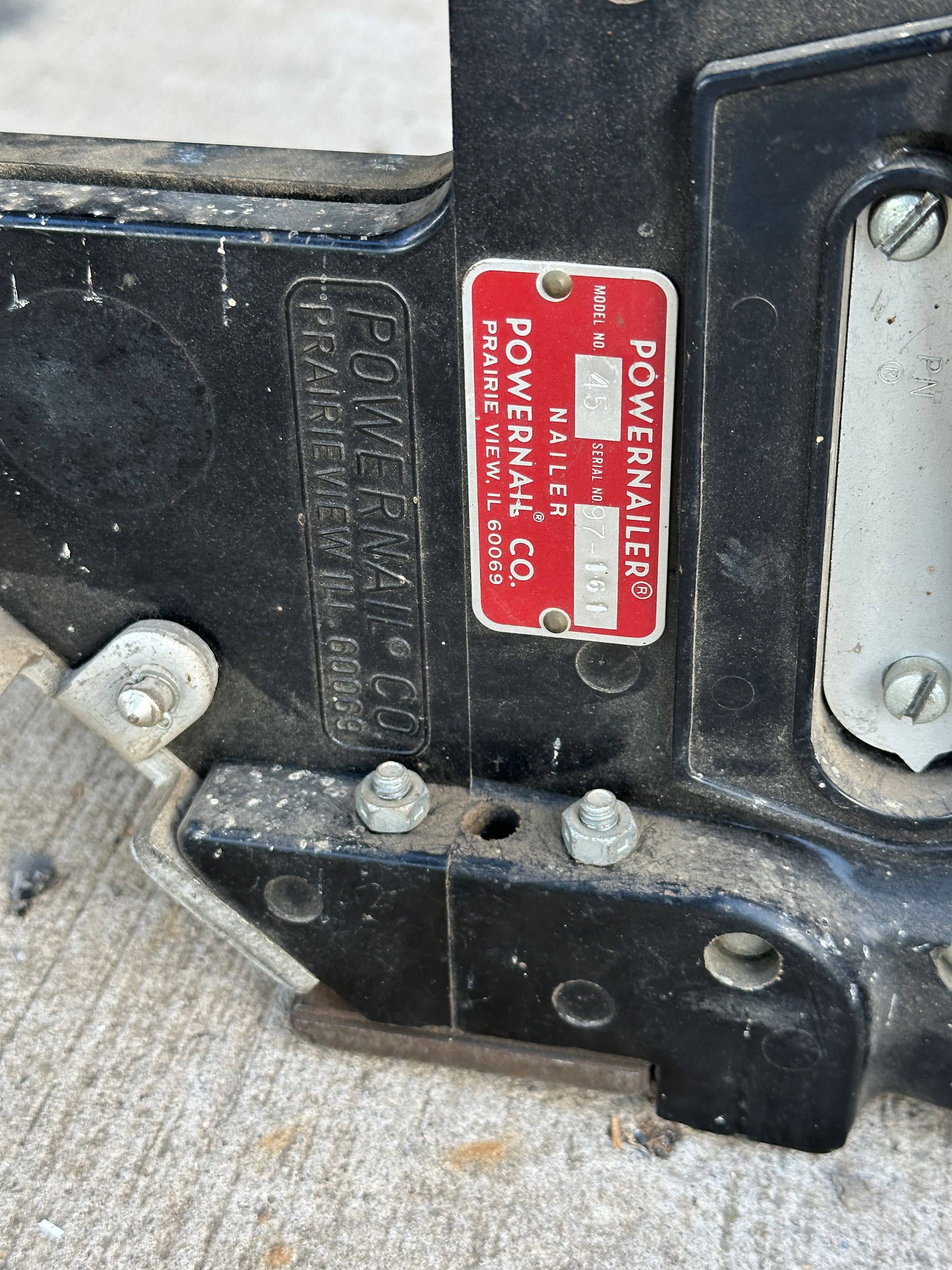 Close-up of a red metal identification plate on a black vehicle frame with bolts and rust
