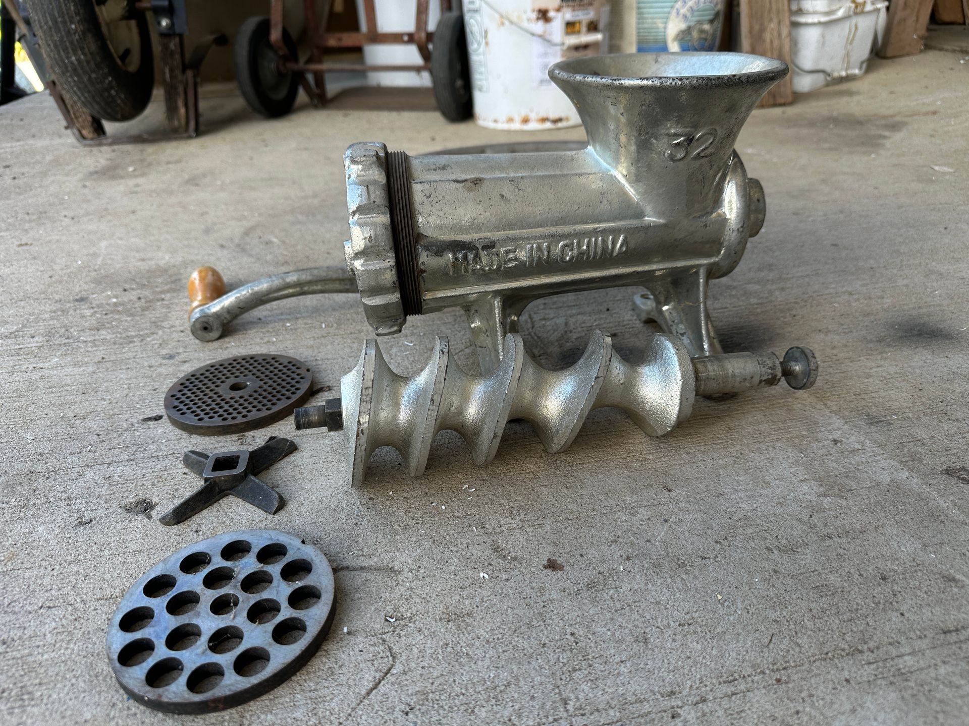 Metal meat grinder on a concrete floor with detached plates and parts nearby