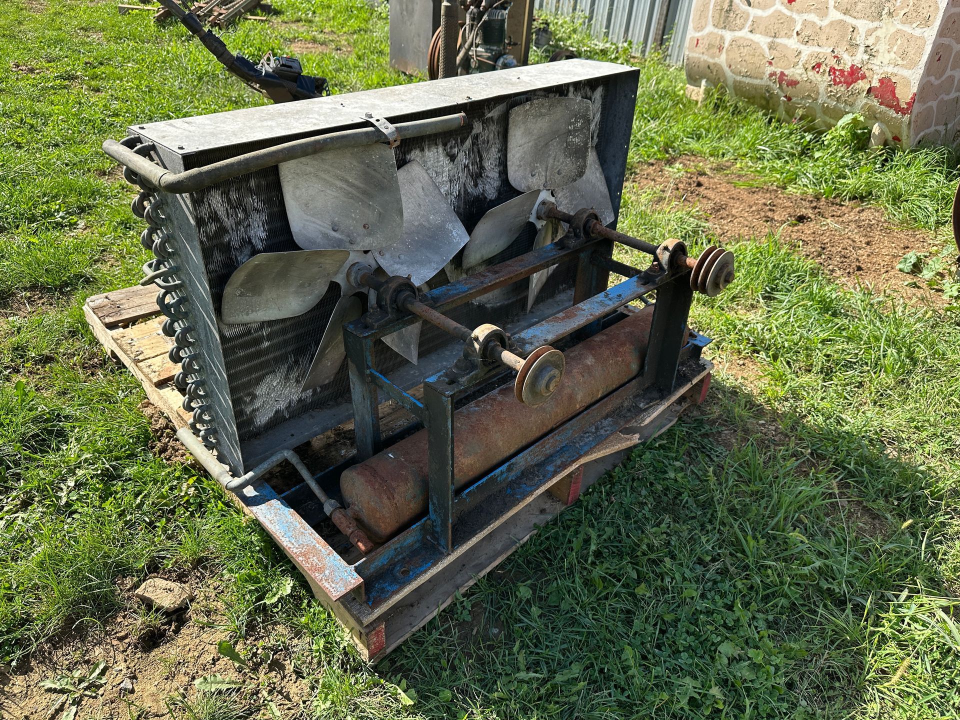 Rusty old machinery on grass beside a stone wall, with metal frame and broken concrete panels